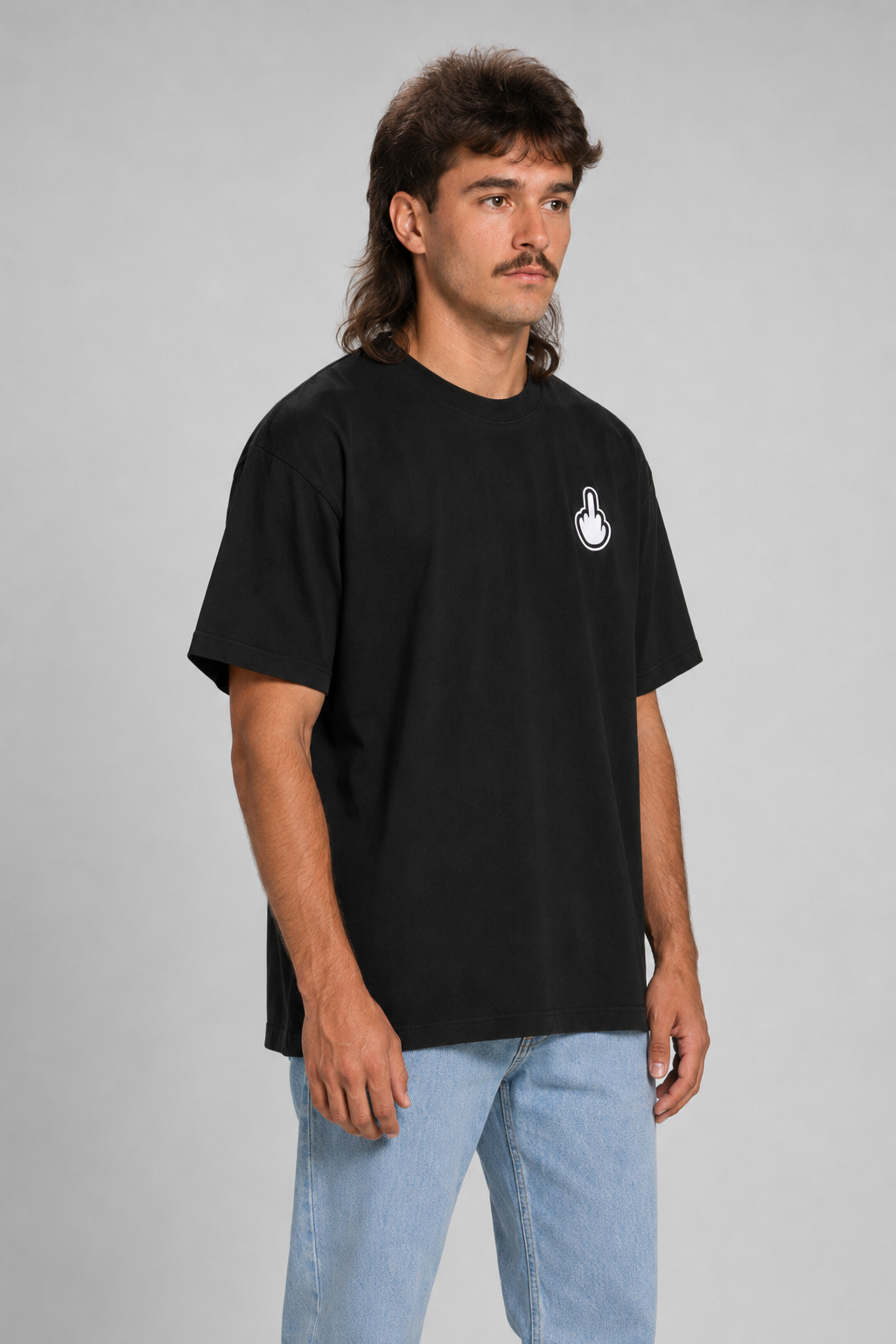 A man wearing a black short-sleeve t-shirt with a small white graphic on the left chest, paired with light blue jeans, standing against a neutral gray studio background. #black